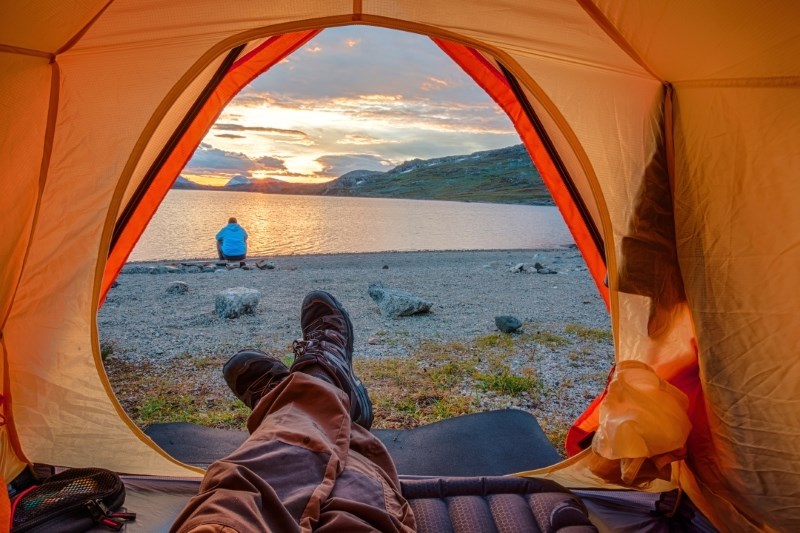 Person relaxing in orange tent beside lake at sunset