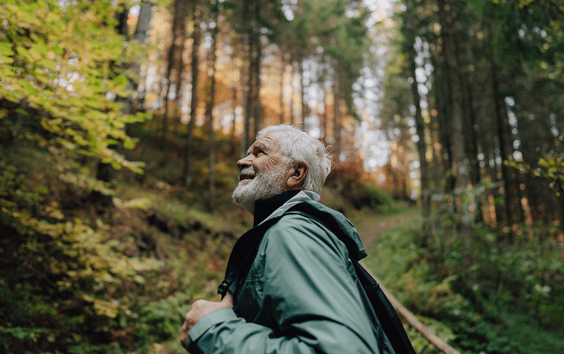 senior man with bag walking through the woods